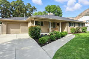 Ranch-style house with a porch, a mountain view, a garage, a chimney, and stucco siding