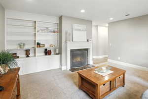 Living room with light carpet, recessed lighting, a glass covered fireplace, and built in features