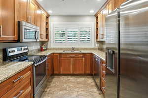 Kitchen featuring appliances with stainless steel finishes, open shelves, light stone countertops, stone finish flooring, and brown cabinets