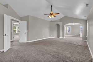 Carpeted empty room with vaulted ceiling, a ceiling fan, and arched walkways