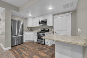 Kitchen featuring stainless steel appliances, white cabinets, dark wood-style flooring, and light stone counters