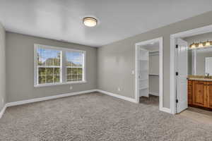 Unfurnished bedroom featuring ensuite bath, light carpet, and a spacious closet
