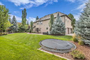 Rear view of house featuring a patio, a yard, a trampoline, and stucco siding