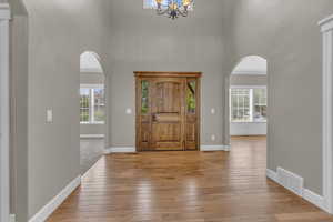 Entryway with a high ceiling, light wood finished floors, arched walkways, and a chandelier