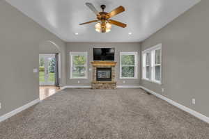 Unfurnished living room featuring carpet, french doors, arched walkways, a stone fireplace, and ceiling fan