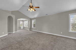 Empty room with lofted ceiling, light colored carpet, arched walkways, plenty of natural light, and ceiling fan