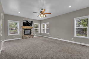 Unfurnished living room featuring light colored carpet, a stone fireplace, a ceiling fan, and recessed lighting