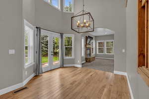 Entrance foyer featuring plenty of natural light, french doors, a towering ceiling, light wood finished floors, and a stone fireplace