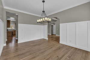 Unfurnished dining area featuring arched walkways, light wood-type flooring, crown molding, and a chandelier