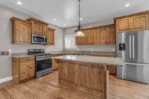 Kitchen with appliances with stainless steel finishes, brown cabinets, light stone counters, a breakfast bar area, and recessed lighting