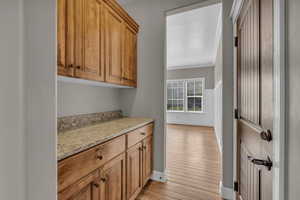 Bar area with light stone counters, brown cabinets, light wood-style flooring, and ornamental molding