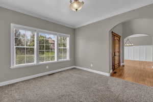 Spare room featuring light carpet, ornamental molding, arched walkways, and a chandelier