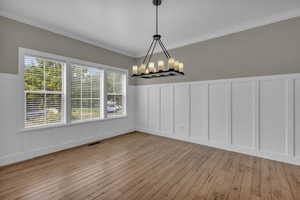 Unfurnished dining area with a decorative wall, ornamental molding, a wainscoted wall, light wood-type flooring, and a chandelier