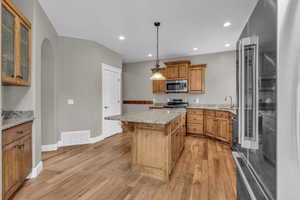 Kitchen with stainless steel appliances, light wood-type flooring, arched walkways, recessed lighting, and light stone countertops
