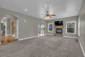 Unfurnished living room featuring light carpet, ceiling fan, a fireplace, recessed lighting, and arched walkways