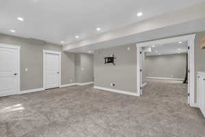 Finished below grade area featuring light colored carpet and recessed lighting