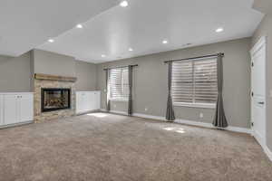 Unfurnished living room with light colored carpet, a stone fireplace, and recessed lighting