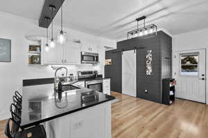 Kitchen with a barn door, white cabinets, light wood-style floors, wood walls, and appliances with stainless steel finishes