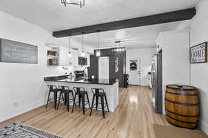 Kitchen featuring white cabinetry, a peninsula, beamed ceiling, light wood-style floors, and a breakfast bar