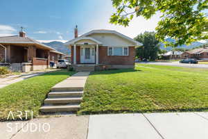 View of front of house with brick siding, a front yard, a mountain view, and a chimney