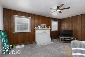 Carpeted living room with wood walls, a textured ceiling, and ceiling fan