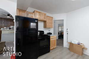 Kitchen with black appliances, a textured ceiling, light brown cabinets, light wood finished floors, and a ceiling fan