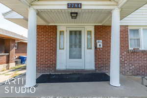 Entrance to property with a porch and brick siding
