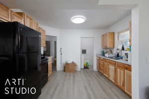 Kitchen featuring black appliances, light countertops, light wood-style floors, light brown cabinetry, and a textured ceiling