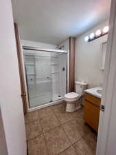 Bathroom with vanity, a shower stall, light tile patterned floors, and a textured ceiling
