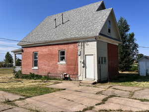 Rear view of property with a lawn, roof with shingles, brick siding, and an outdoor structure