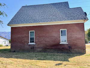 View of side of property with roof with shingles, brick siding, and a lawn