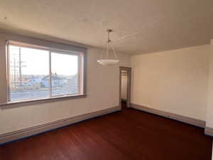 Unfurnished dining area featuring a baseboard radiator, baseboard heating, dark wood-type flooring, and a textured ceiling