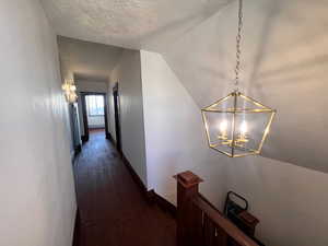 Corridor featuring dark wood-style floors, a chandelier, vaulted ceiling, a textured ceiling, and an upstairs landing