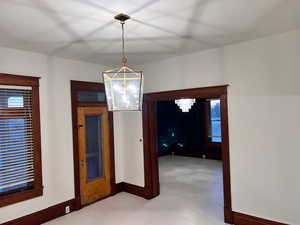 Unfurnished dining area featuring baseboards and a chandelier