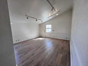 Spare room featuring a textured wall, rail lighting, wood finished floors, and vaulted ceiling