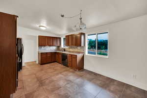 Kitchen with tasteful backsplash, brown cabinets, dark tile patterned flooring, black appliances, and light stone counters
