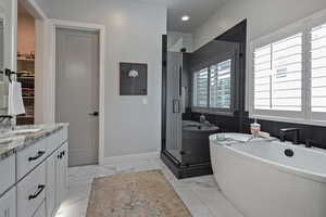Full bath with vanity, a shower stall, a soaking tub, and light marble finish flooring