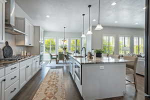 Kitchen with a kitchen breakfast bar, dark stone counters, wall chimney range hood, hanging light fixtures, and a textured ceiling
