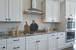 Kitchen featuring wall chimney range hood, white cabinetry, appliances with stainless steel finishes, dark stone countertops, and dark wood-style floors