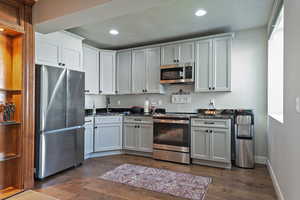 Kitchen featuring stainless steel appliances, dark wood-style floors, dark stone countertops, recessed lighting, and a textured ceiling