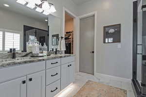 Full bath with a stall shower, double vanity, and a walk in closet