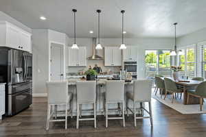 Kitchen with stainless steel fridge, a kitchen island with sink, light stone countertops, dark wood-style floors, and recessed lighting