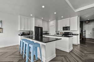 Kitchen with a kitchen island with sink, freestanding refrigerator, white cabinets, a breakfast bar area, and recessed lighting