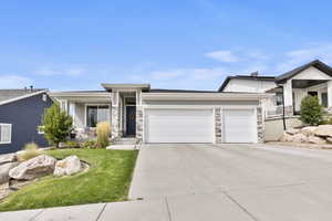 View of front of property with stone siding, an attached garage, concrete driveway, a front yard, and covered porch