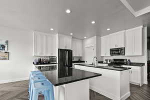 Kitchen featuring stainless steel appliances, white cabinets, a breakfast bar area, recessed lighting, and dark stone counters
