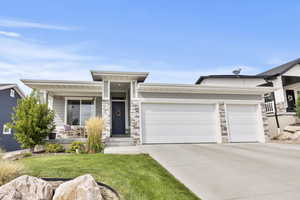 View of front of home with concrete driveway, a garage, stone siding, covered porch, and a front lawn