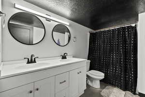 Bathroom with a textured ceiling, double vanity, and concrete floors