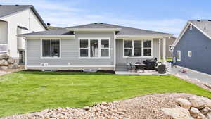 Back of property with a shingled roof, a patio, and a lawn