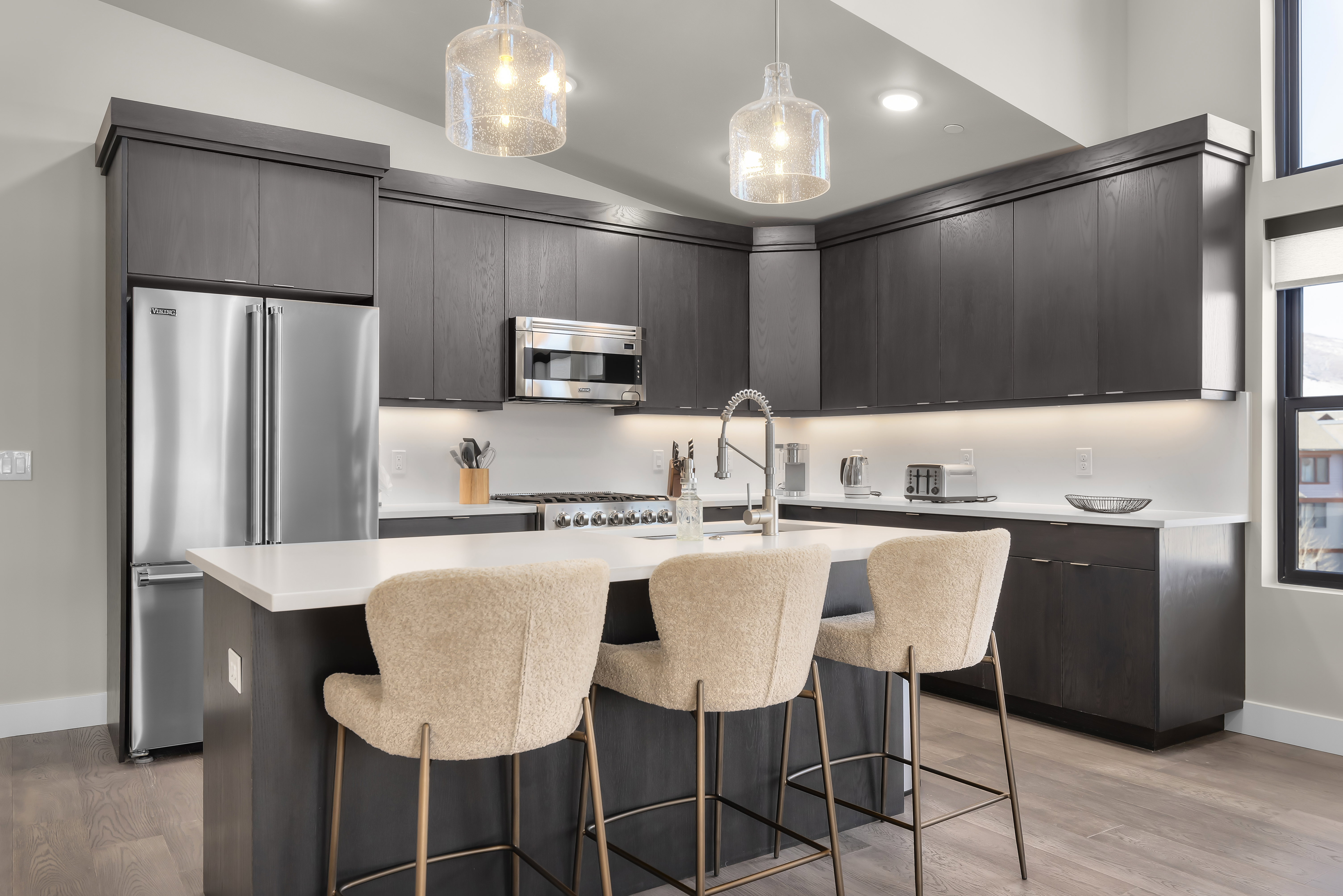 Kitchen with a kitchen island with sink, modern cabinets, light wood-style floors, stainless steel appliances, and decorative light fixtures