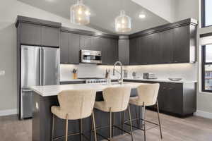 Kitchen with a kitchen island with sink, modern cabinets, light wood-style floors, stainless steel appliances, and decorative light fixtures